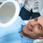 Mature male in a dental chair looking in a mirror, smiling
